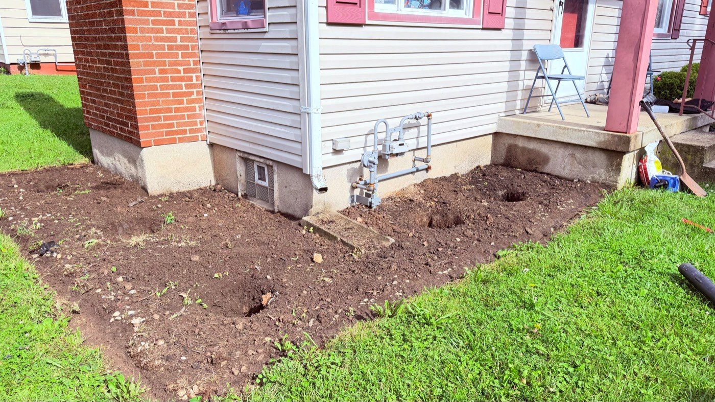 Bare dirt planting bed before mulch installation along the brick foundation of a home