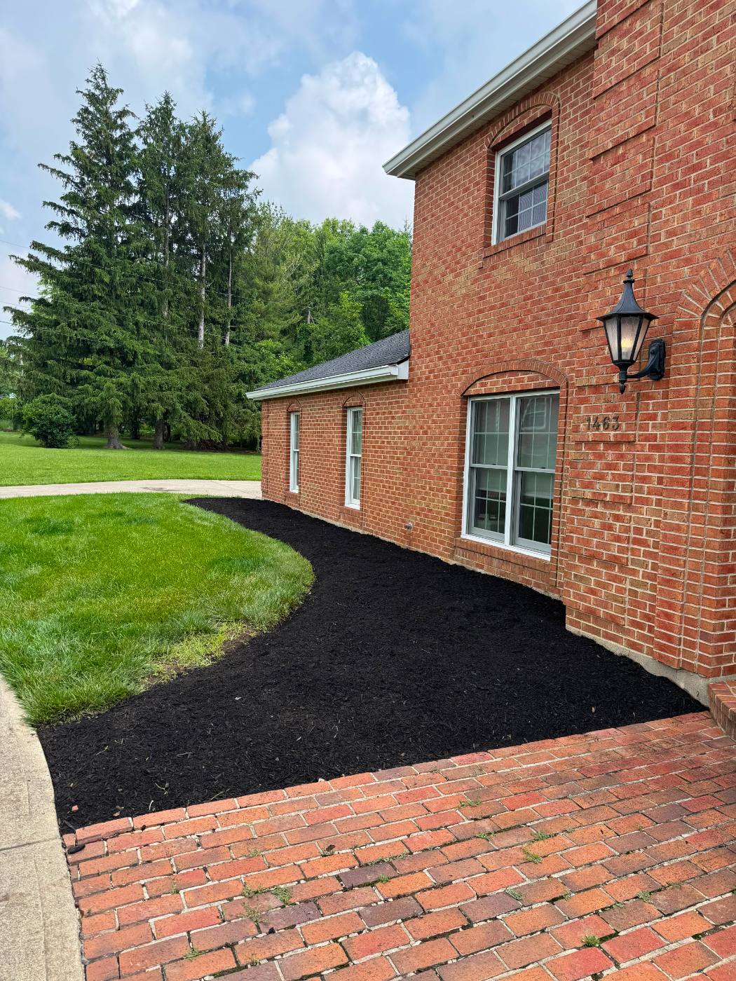 Mulch installation service — curved black mulch landscape bed along brick home